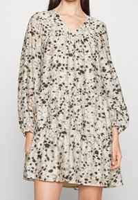Robe imprimée florale dans des tons beige clair et olive, avec un décolleté en V, de longues manches bouffantes et une jupe à volants avec une coupe décontractée.