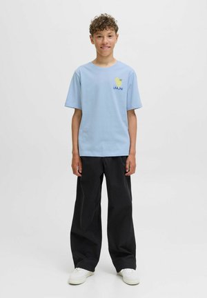 Lichtblauwe katoenen T-shirt met korte mouwen, met een gele citroengrafiek en de tekst "LIMONE". Gecombineerd met losse zwarte broeken en witte sneakers.