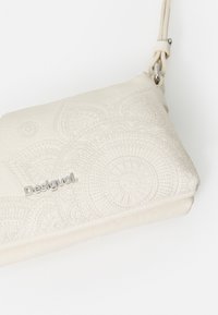Witte clutchtas met reliëf ronde patronen, voorzien van een zilveren logo en een gevlochten band. Gladde textuur met een ritsluiting.