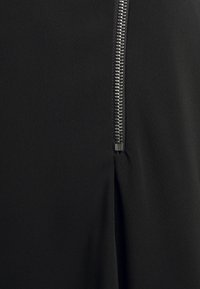 Zwarte kledingstof met een soepele textuur; voorzien van een metalen rits aan de zijkant met zichtbare tanden en een slanke trekker.