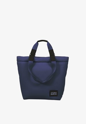 Granatowa torba na ramię z wyściełanego materiału, z podwójnymi uchwytami z czarnymi elementami oraz widoczną metką "STUDIO BERLIN" z boku.