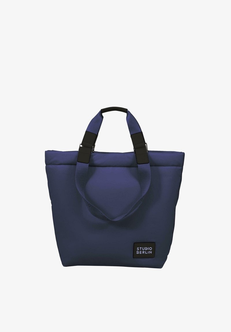 Sötétkék vászontáska párnázott anyagból, dupla fogantyúkkal, fekete hardverrel, és egy jól látható "STUDIO BERLIN" címkével az oldalán.
