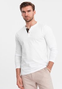 Weißes Langarm-Henley-Shirt mit schwarzem Knopfverschluss und drei braunen Knöpfen. Weiches Material, taillierter Schnitt und Rundhalsausschnitt.