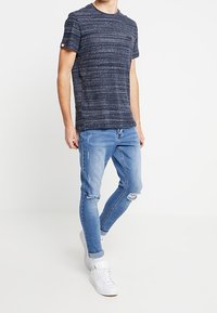 Námořnické pruhované tričko s krátkým rukávem a kulatým výstřihem, doplněné o světle modré zúžené džíny s otvory a bílé tenisky.