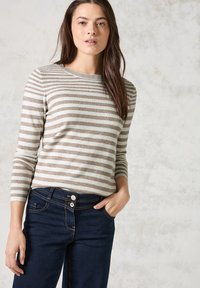 Pull rayé beige et crème, col rond, manches ajustées. Assorti à un jean bleu foncé avec fermeture à deux boutons et poches latérales.