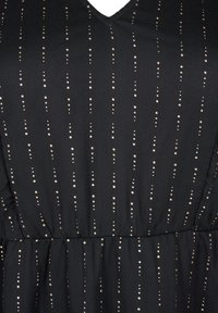 Svart klänning med V-ringning, texturerad tyg, prydd med vertikala gyllene prickar och mellanrumslinjer över hela ytan, med en samlad midja.