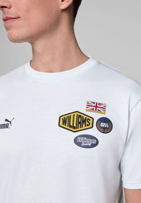 Jasnoniebieski bawełniany T-shirt z okrągłym dekoltem, z haftowanymi naszywkami: "WILLIAMS", brytyjska flaga oraz "EST. 1977" w granatowym i żółtym kolorze.