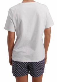Camiseta de algodón blanca de manga corta, vista desde la parte posterior. Combinada con pantalones cortos de color marino con un diseño geométrico.