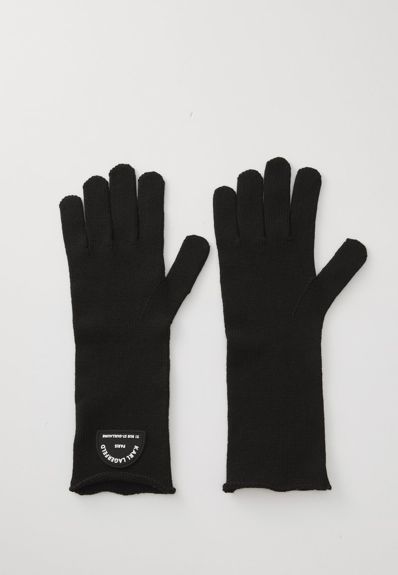 Sorte strikkede hansker med forlengede fingre, sømløst design, og et merketikett på håndleddet. Materialet ser mykt ut med en teksturert finish.