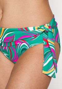 Parte de baixo de biquíni verde com um design drapeado, apresentando padrões coloridos em espiral nas cores rosa, laranja e branco. Inclui um detalhe atado na lateral.