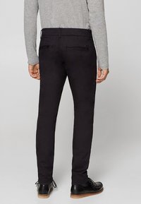 Pantaloni neri slim-fit con due tasche posteriori, realizzati in un tessuto morbido. Abbinati a una maglia grigia a maniche lunghe e scarpe eleganti nere.