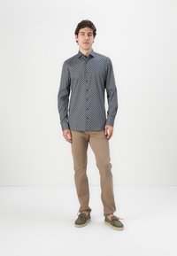 Long-sleeve, button-up shirt in navy with a geometric pattern, paired with tan pants and green boat shoes with orange laces.
