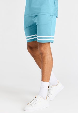 Helle blaue Sportshorts mit weißen horizontalen Streifen am Saum, kombiniert mit weißen Turnschuhen und knöchellangen Socken.