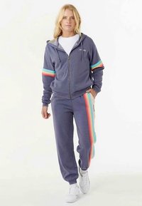 Gemêleerde paarse zip-up hoodie met kleurrijke gestreepte accenten op de mouwen, gecombineerd met bijpassende joggingbroek met strepen aan de zijkanten.