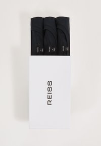 Drei gefaltete schwarze T-Shirts mit sichtbaren Nackenetiketten in einer weißen Schachtel mit der Aufschrift „REISS“ auf einfachem Hintergrund.