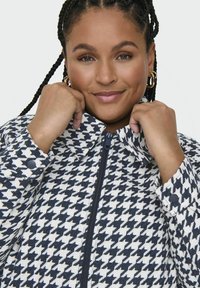 Płaszcz w deseń pepitki w kolorze granatowym i białym, z zamkiem błyskawicznym, stójką i zapinanymi mankietami. Teksturowana tkanina.