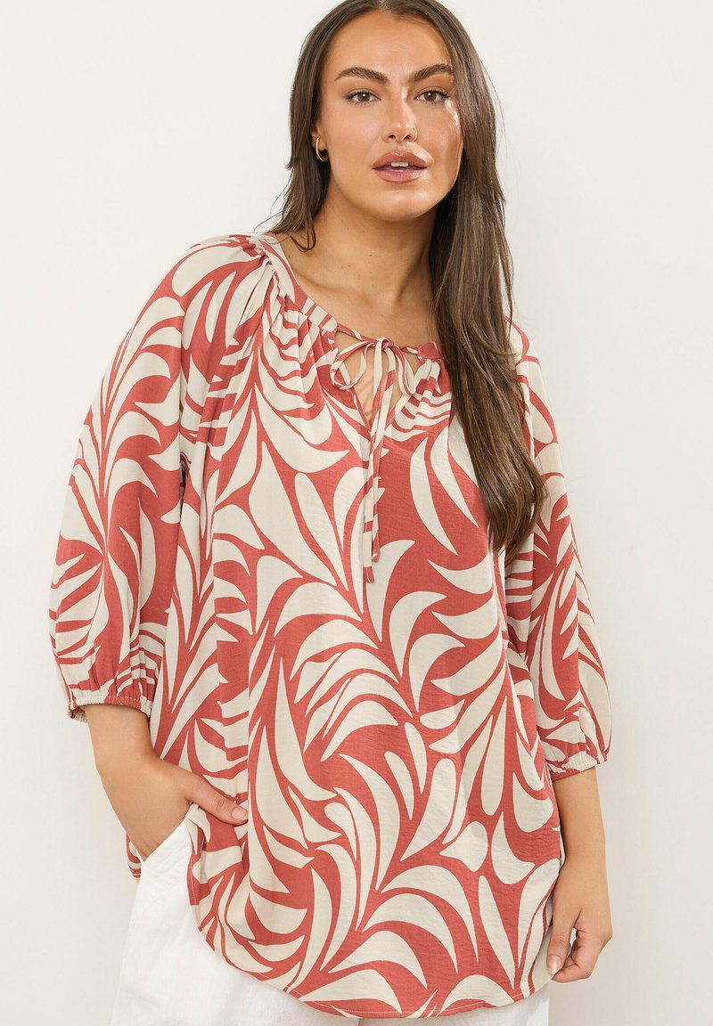 Langarmbluse in Terrakotta und Creme mit floralem Muster, ausgestattet mit einem Bindekragen und gerafften Ärmeln, aus leichtem Material gefertigt.