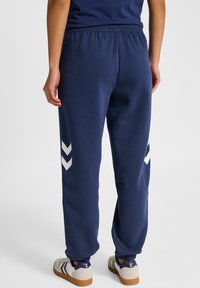 Granatowe dresy z elastycznym pasem, z białymi wzorami w zygzak na zewnętrznej stronie każdej nogawki. Miękka tkanina; zwężane u kostek.