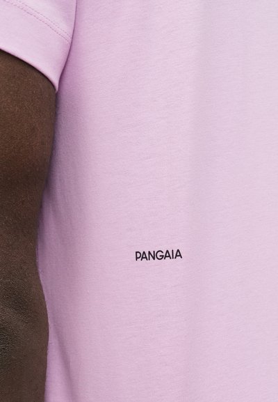 Κοντινό πλάνο στο χέρι και στον κορμό ενός ατόμου που φοράει ένα ανοιχτό μοβ T-shirt με μικρό μαύρο κείμενο «PANGAIA» στο στήθος.