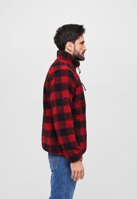 Rød og sort ternet fleecejakke med høj krave, frontlynlås og sidelommer, paired med blå jeans.