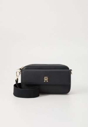 Sac à bandoulière en cuir noir avec quincaillerie dorée, fermeture éclair et une bandoulière noire amovible. Présente un logo en relief à l'avant.