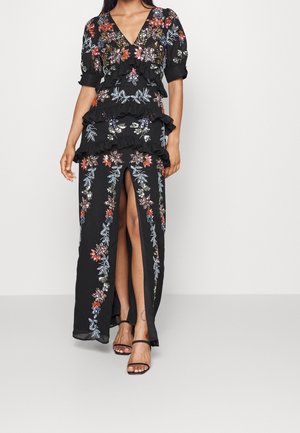 Mustapuku, jossa on punaisia, sinisiä ja vihreitä kukka-ompeluja. Ominaisuuksiin kuuluu röyhelökerroksia ja V-pääntie, sivuhalkio sekä avonaiset hihat.