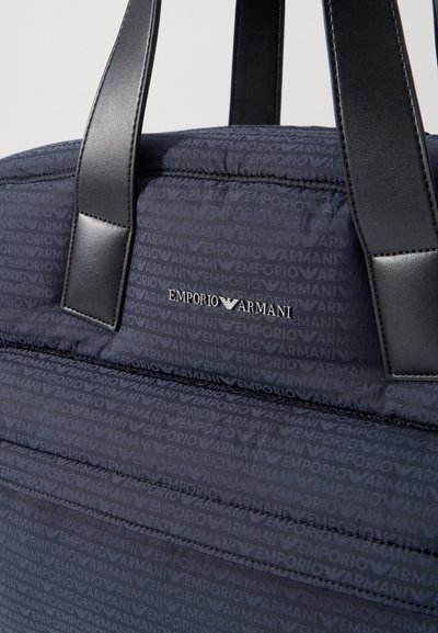 Mornarsko modra prešita torba z črnimi usnjenimi detajli, ki se ponaša z celovitim vzorcem logotipa Emporio Armani in trdnimi, gladkimi ročaji.