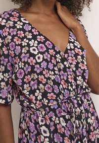 Robe fleurie avec un col en V profond, manches courtes, fond noir, et motifs floraux violets, roses et blancs. Comprend une ceinture à la taille et des boutons.