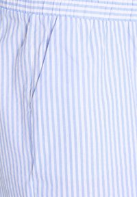 Tessuto a righe blu chiaro e bianco con una consistenza morbida. Presenta pieghe e una vita elastica. Le righe verticali creano un design semplice.