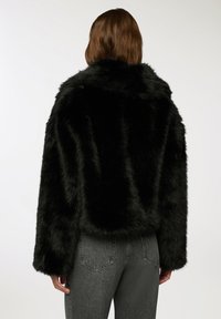 Czarna kurtka z sztucznego futra, krótka, z szerokim kołnierzem, teksturowaną powierzchnią, długimi rękawami i prostym wzorem. Noszona z szarymi dżinsami.