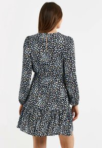 Vestido negro con un dobladillo con volantes, que presenta un colorido patrón floral. Mangas largas y un detalle de abertura en la espalda. Textura de tela suave.