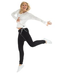 White long-sleeve top with round neckline paired with black joggers featuring drawstring waist. White athletic shoes. Background is plain white.
