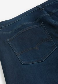 Jeans din denim de culoare albastru închis, cu o buzunar posterior cu cusături contrastante. Textură netedă și design conic, cu bucle standard pentru centură.
