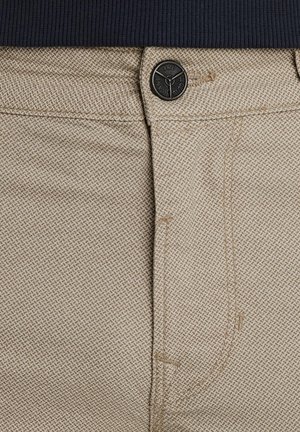 Bež hlače od teksturirane tkanine s crnim kopčanjem i suptilnim dijagonalnim uzorkom. Pojas je od tamnoplave rebraste tkanine.