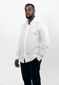 Witte lange mouwen blouse met een iets gestructureerde kraag, gecombineerd met donkere trousers. Glad stof, aangesloten ontwerp, minimale versieringen.
