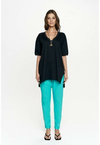 Czarny luźny top z krótkimi rękawami, w połączeniu z tealistymi, zwężającymi się spodniami. Modelka nosi czarne sandały i naszyjnik z warstw.