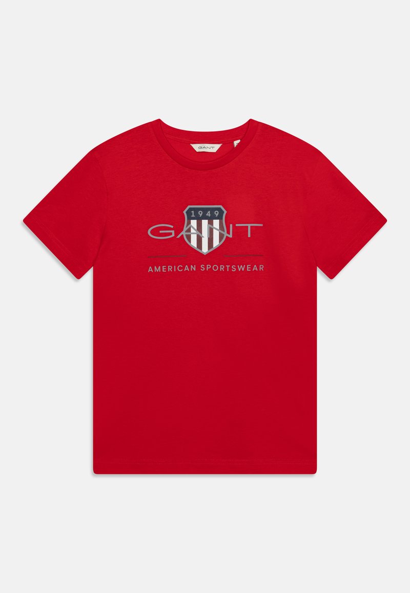 Camiseta de algodón roja con un logo impreso que presenta un diseño de escudo y el texto "GANT AMERICAN SPORTSWEAR" debajo, con cuello redondo y mangas cortas.
