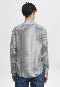 Camisa de botones a rayas en lino azul claro y blanco, con mangas largas, cuello y un dobladillo curvado con puños abotonados.