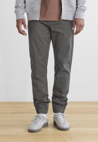 Gray jogger pants with elastic cuffs, made of lightweight material, paired with gray sneakers and a light gray zip-up hoodie.