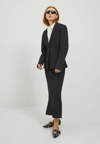 Blazer nero su misura con un solo bottone, abbinato a una gonna nera aderente e delle ballerine nere a fantasia con fiocchi. Design elegante e minimal.