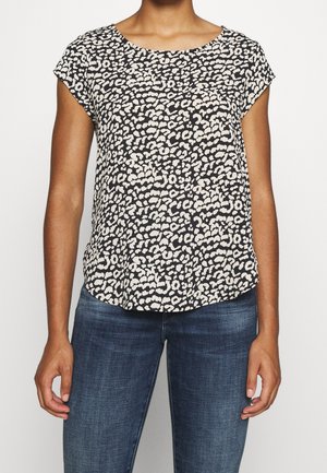 Kvinde iført en kortærmet bluse med sort-hvidt leopardprint kombineret med mørkeblå jeans.
