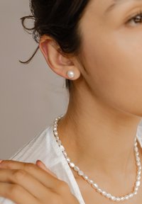 Orecchini di perle bianche e una collana abbinata presentano un design classico. Le perle hanno una superficie liscia e lucida e sono di forma irregolare.