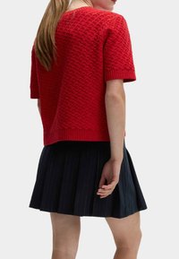 Czerwony sweter dzianinowy z krótkim rękawem, z teksturowanym wzorem i ściągaczami, zestawiony z plisowaną ciemnonawową spódnicą w paski.