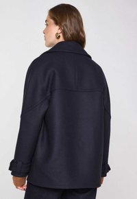 Donkerblauw wollen jas met een gestructureerde kraag, zijzakken en opgerolde manchetten. Heeft een gladde textuur en een relaxte pasvorm, met minimale stiksels.