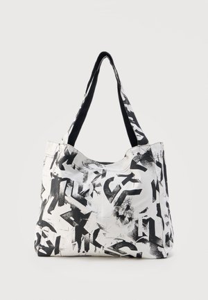 Bolsa tote blanca con letras negras en estilo grafiti abstracto y correas anchas para el hombro sobre un fondo claro y uniforme.