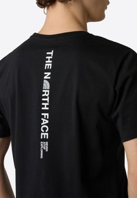 Crni pamukasti majica s vertikalnim bijelim logotipom na leđima koji glasi "THE NORTH FACE" i "NEVER STOP EXPLORING."