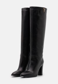 Bottes en cuir noir montantes avec une finition lisse, bout pointu et un talon bloc haut. Présente un accent doré métallisé en forme de "T" sur le côté.