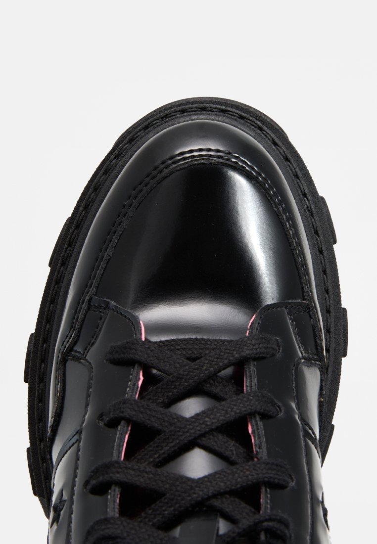 Czarne skórzane trampki o błyszczącym wykończeniu, z grubą gumową podeszwą i kontrastującym różowym przeszyciem na sznurówkach. Okrągły nosek, wyściełany kołnierz.