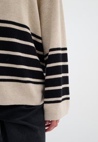 Beige en zwart gestreepte trui met een relaxte pasvorm. De stof lijkt zacht en heeft brede zwarte strepen, met een geribbelde onderrand en mouwen.