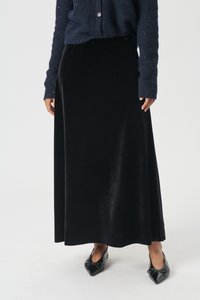 Črna žametna maxi krilo z gladko teksturo, ki ima oprijet pas in tekoč silhuet, v paru s črnimi koničastimi balerinkami in mornarsko modrim kardiganom.